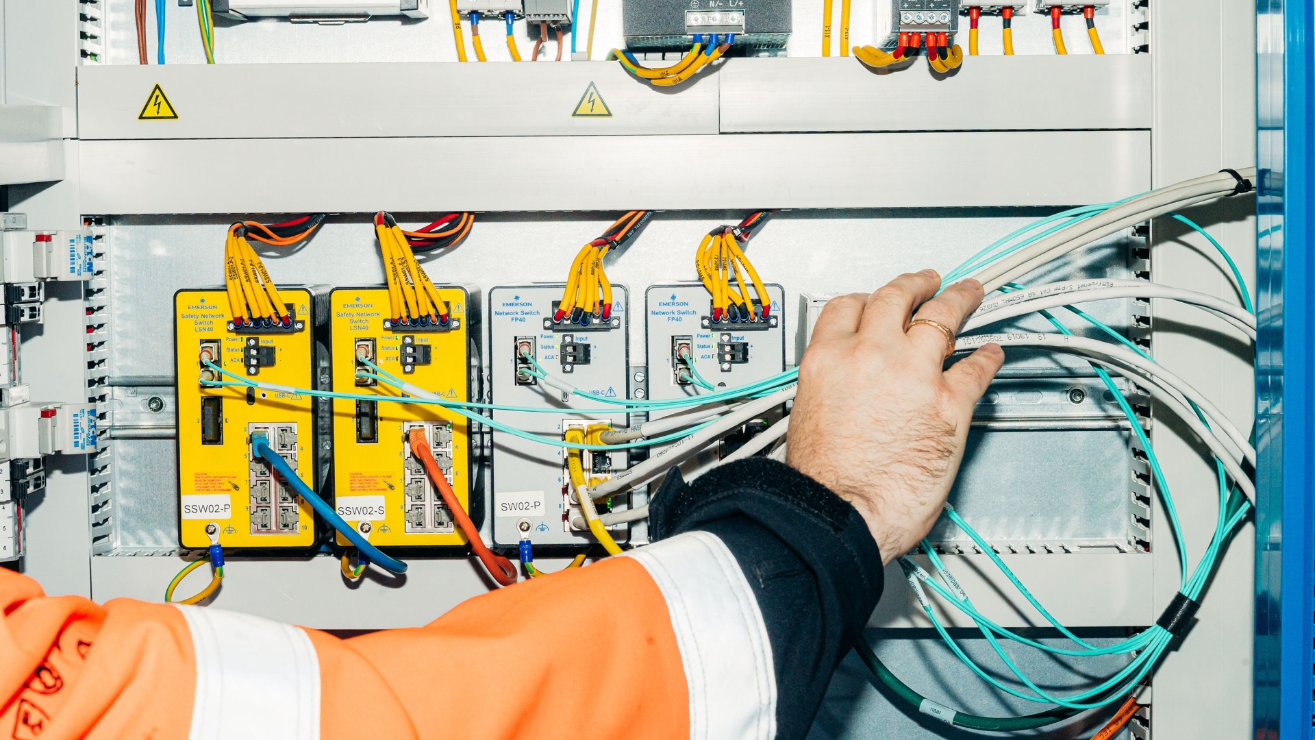 Een hand begeleidt kabels in een soort meterkast