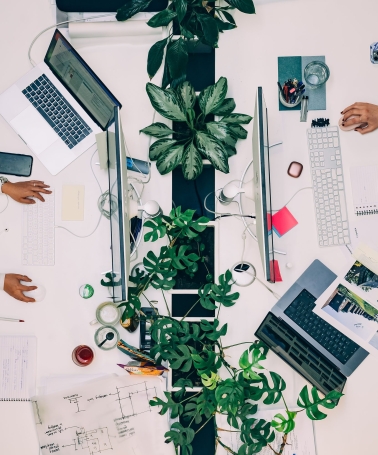 Twee mensen werken tegenover elkaar aan bureaus. Van bovenaf gefotografeerd.