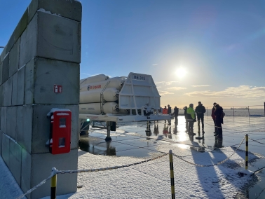 Groep mensen staat bij een Air Liquide tank op een besneeuwd industrieel terrein.