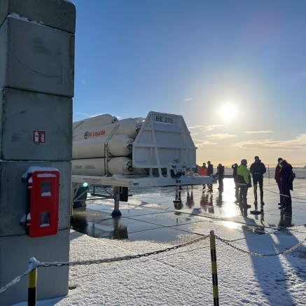 Groep mensen staat bij een Air Liquide tank op een besneeuwd industrieel terrein.
